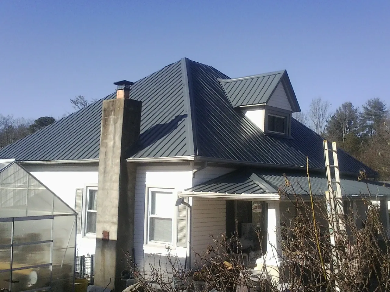 Dark blue standing seam metal roof on a white farmhouse with dormer — Slate & Tile Roof Repair by Roofing Brothers in Lake Grove