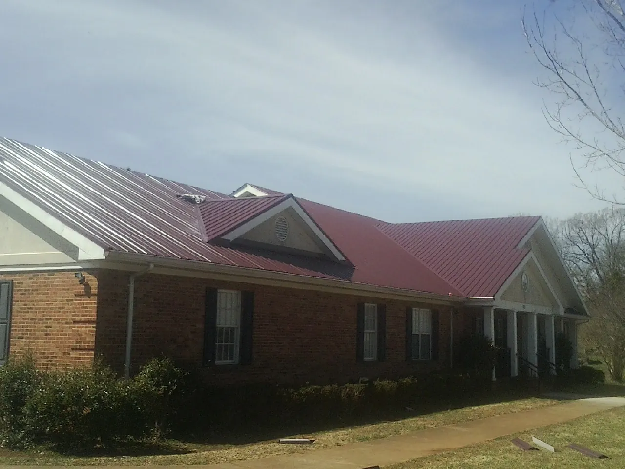 Red metal roof with gabled entries on a long brick building, from a Hail Damage Roof Repair job in Lake Grove