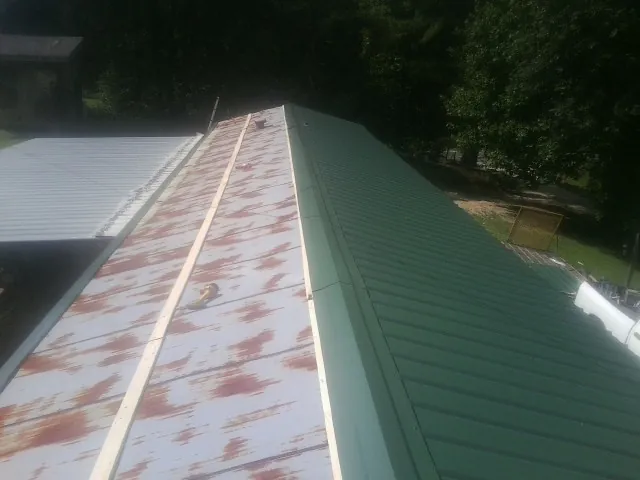 Old rusted panels beside newly installed green metal roofing — Wind Damage Roof Repair by Roofing Brothers in Lake Grove