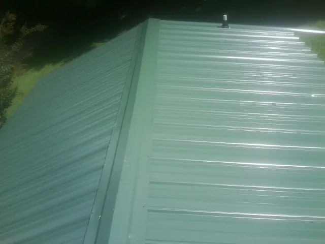 New green metal panels meeting at the ridge of a roof — Flat Roof Repair work by our crew in Lake Grove