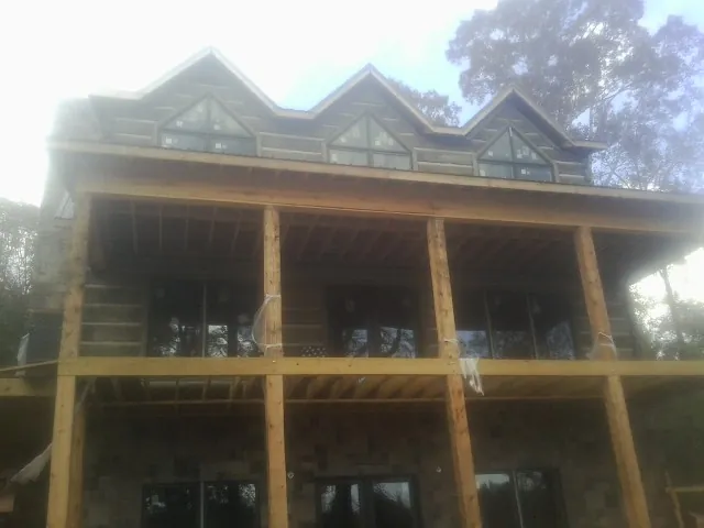Dormers and porch framing on a large log home under construction — Roof Coating work by our crew in Lake Grove