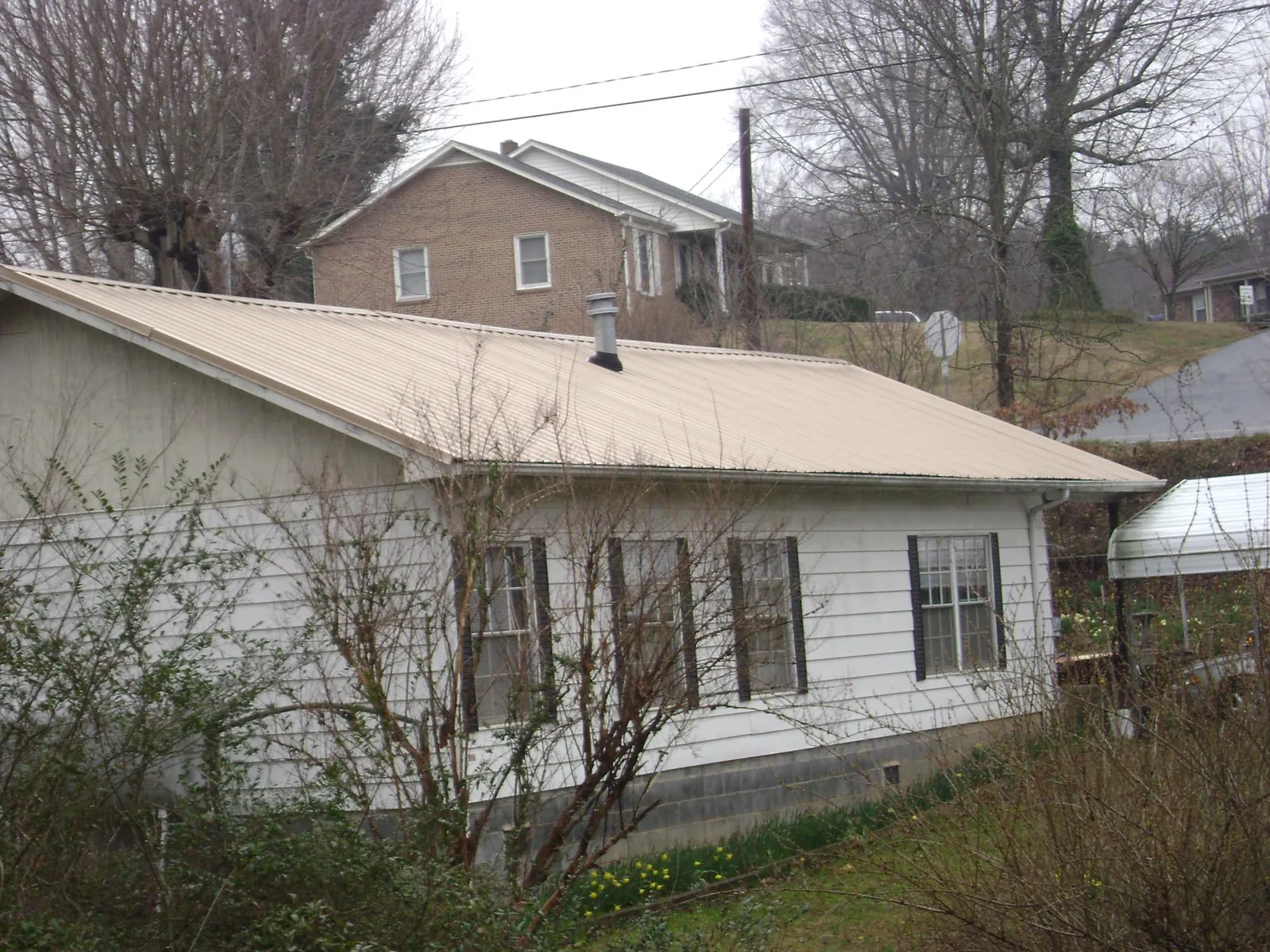 Tan metal roof on a white sided house set into a hillside — Commercial Roofing by Roofing Brothers in Lake Grove