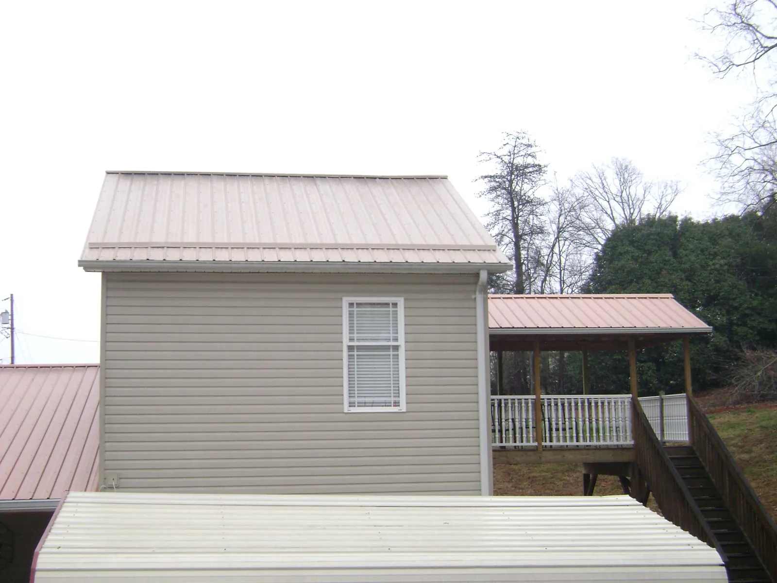 Tan metal roofs on a two story addition and attached porch, from a Roof Replacement job in Lake Grove