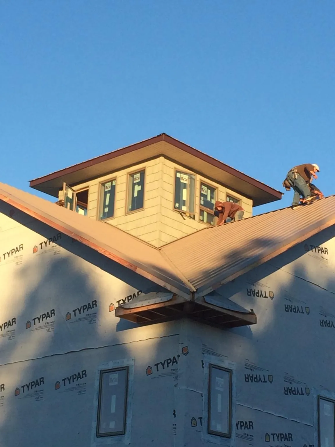 Roofers working around a rooftop cupola on a new metal roof at sunset — Roof Waterproofing in Lake Grove by Roofing Brothers